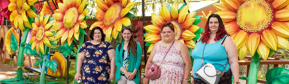 Four ladies from Optimae's Community Integration program pose in front of a sunflower art installation at the Blank Park Zoo in Des Moines.